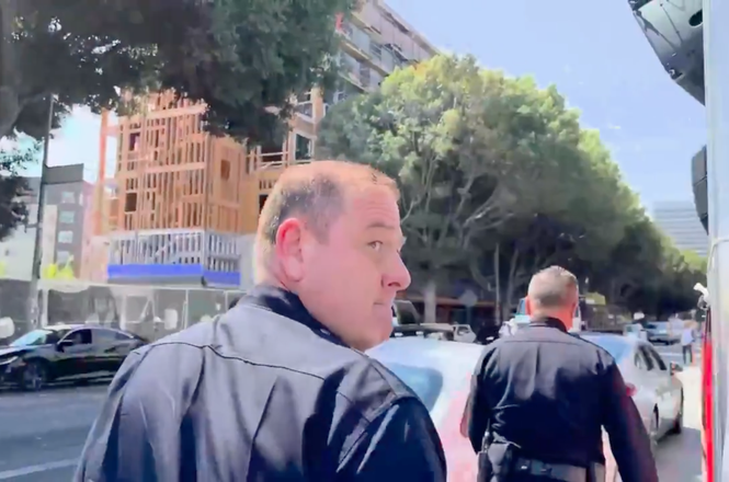 A police officer turns toward freelancer Sean Beckner-Carmitchel moments before shoving the journalist, who was reporting on a pro-immigrant car caravan in downtown Los Angeles, California, on Aug. 12, 2025.