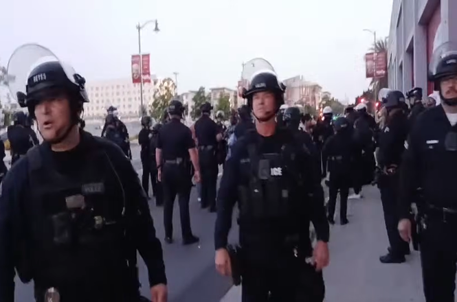 Officers prevent press from approaching a kettled crowd of protesters and journalists in downtown Los Angeles, California, on May 1, 2026. Livestreamer Gonzalo Gonzalez was arrested while filming the police action and charged with failure to disperse.