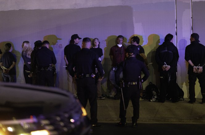 Journalist Sean Beckner-Carmitchel, center in red, was detained alongside other members of the press while documenting immigration protests in Los Angeles on Aug. 8, 2025. Officers also pushed and struck him in the ribs with a baton that evening.
