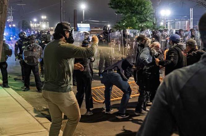 New Jersey State Police officers, at rear with riot shields, spray irritants at protesters and press gathered outside a detention center in Newark on May 29, 2026. Photojournalist Josh Pacheco was sprayed and shot at with crowd-control munitions.