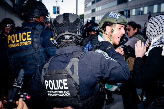 Photojournalist Ethan Cohen, in press helmet at center right, is thrust backward by a Customs and Border Protection officer while covering a workers’ rights and immigration protest in Los Angeles, California, on May 1, 2026.