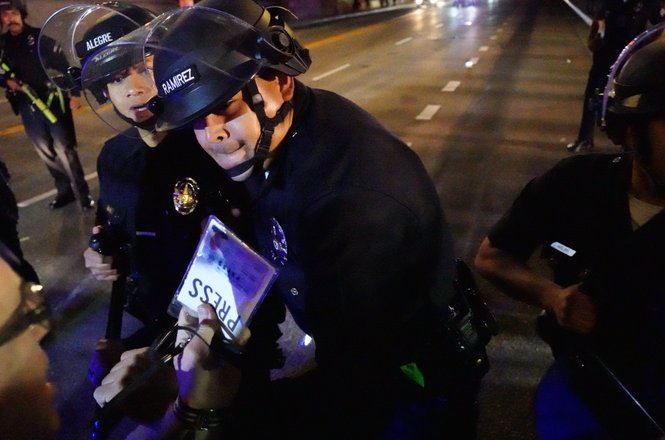 A Los Angeles police officer uses a baton to strike photojournalist Nick Stern, bottom left, as Stern holds up his press credentials amid immigration protests on Aug. 8, 2025. Stern was pushed and struck in the face, and his credentials were damaged.