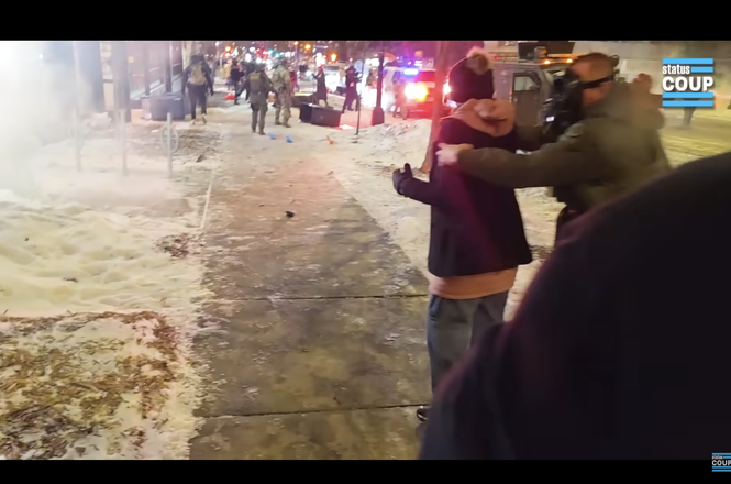 Status Coup reporter Tina-Desiree Berg, in hat at center right, as she is grabbed from behind and thrown to the ground by a federal officer while reporting on a protest outside a hotel in Minneapolis, Minnesota, on Jan. 25, 2026.