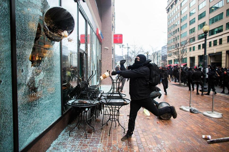demonstrator smashes a Starbucks window using a trash can